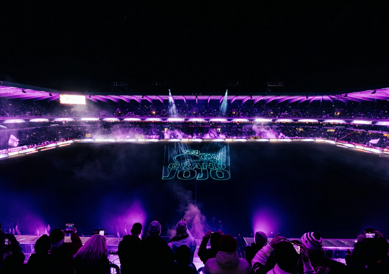 A stadium at night lit purple, with a projected show across the pitch and the perimeter boards glowing